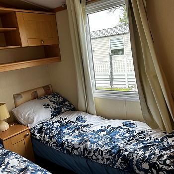 Two single beds with blue bedding inside the green Swift Mosell caravan